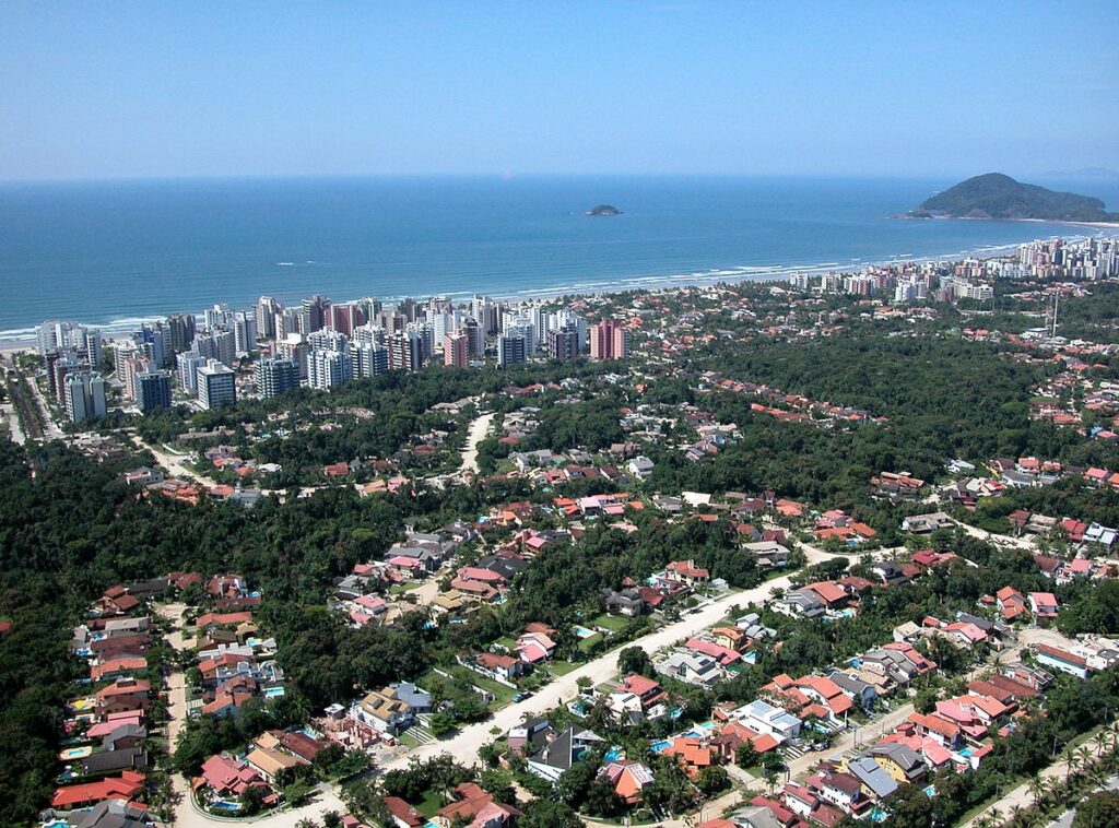 Vista de cima da Riviera de São Lourenço, bairro planejado em Bertioga - São Paulo. À frente da cidade, toda desenhada, há o mar azul.