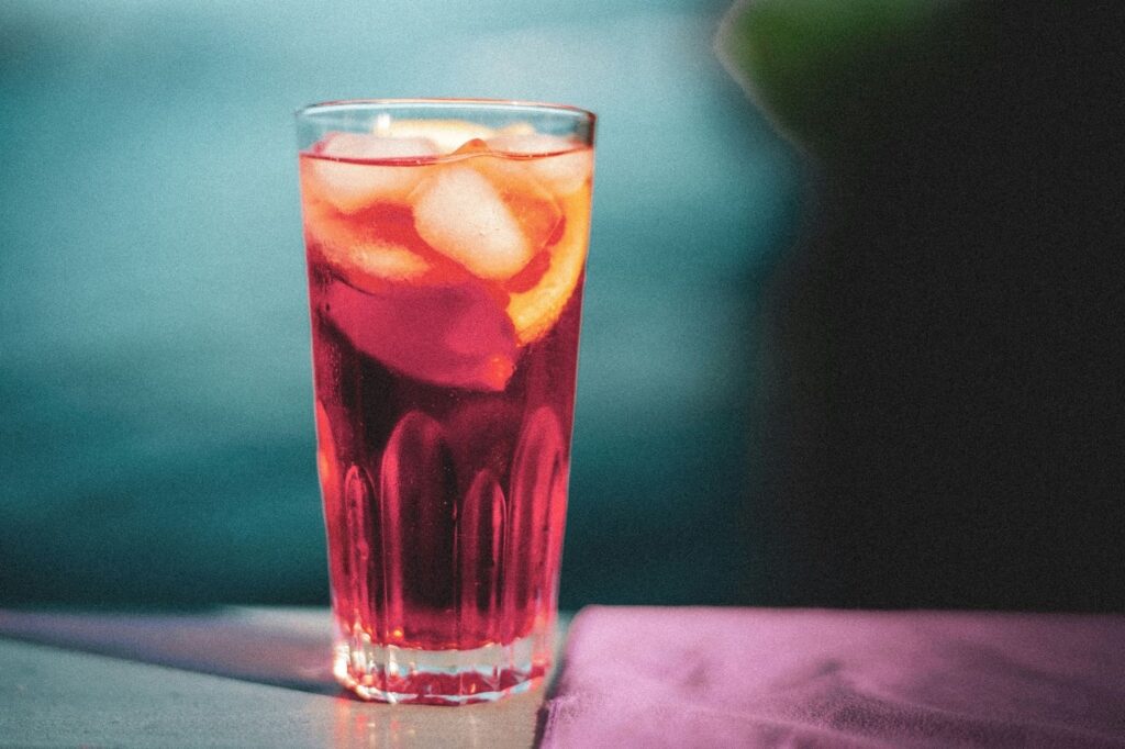 Copo alto de pink lemonade com gelo e rodelas de limão, bebida rosa servida em ambiente iluminado e refrescante.